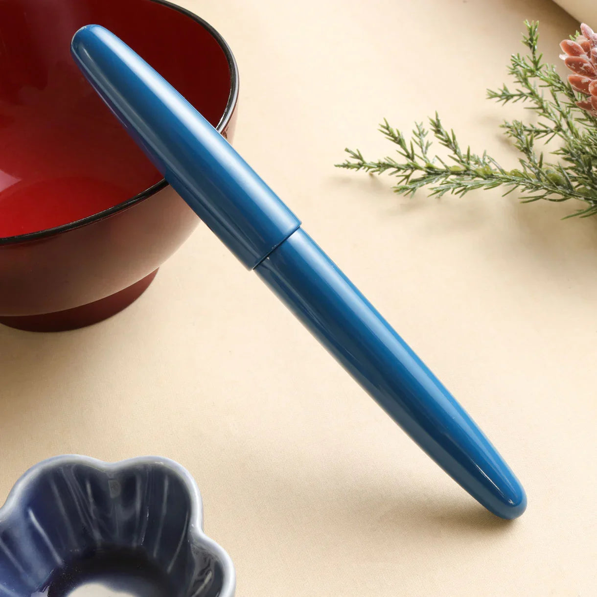 Aizu Urushi Ao fountain pen with a deep blue Urushi lacquer finish leaning against Japanese bowl