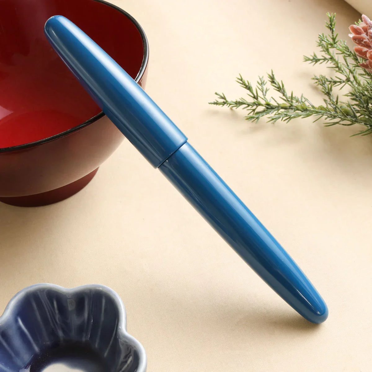 Aizu Urushi Ao fountain pen with a deep blue Urushi lacquer finish leaning against Japanese bowl
