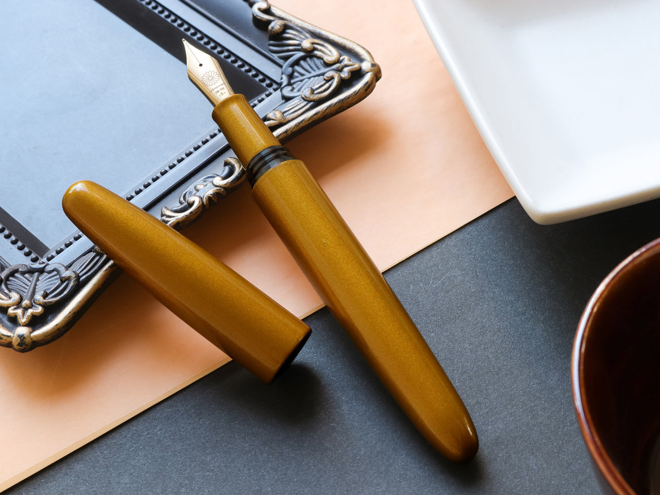Yellow fountain pen on a textured surface with a white plate and decorative items.