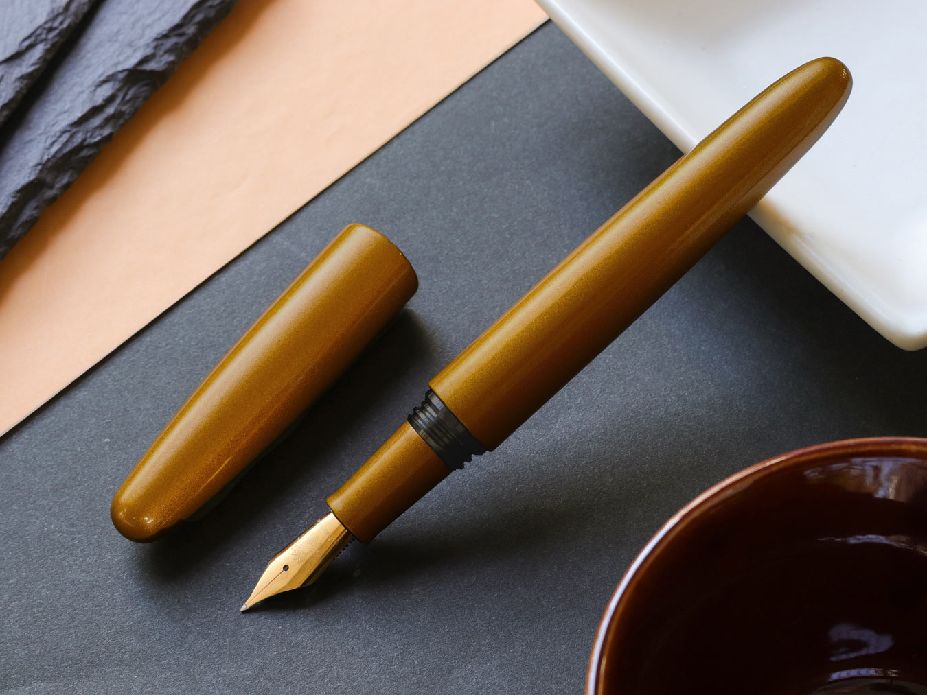 Dark Gold Nashiji fountain pen on a dark surface with a white dish and brown bowl in the background.