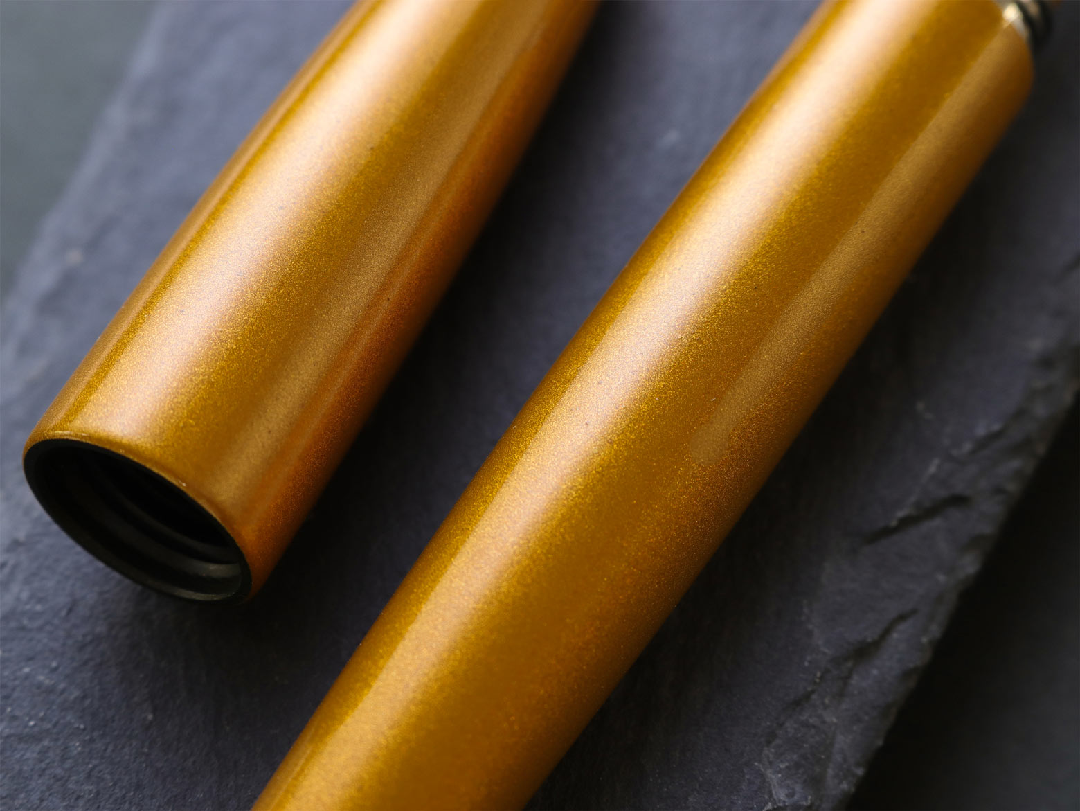 Close up gold-colored fountain pen body on a dark gray surface