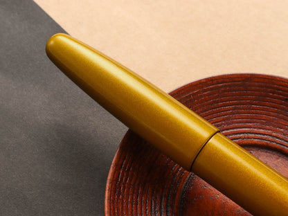 Gold urushi lacquered fountain pen on a textured brown surface with a neutral background