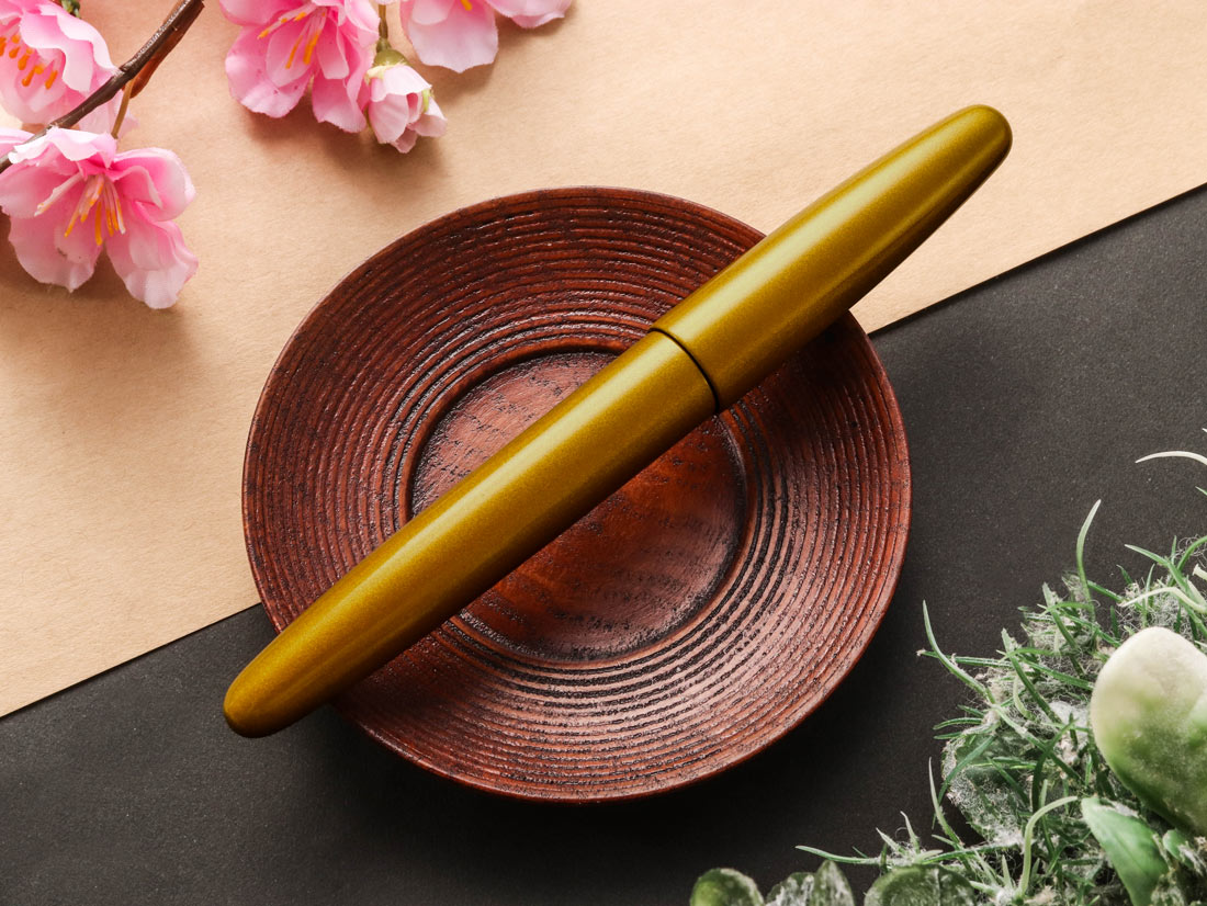 Gold color Urushi pen Nashiji technique on a brown plate with pink flowers in the background