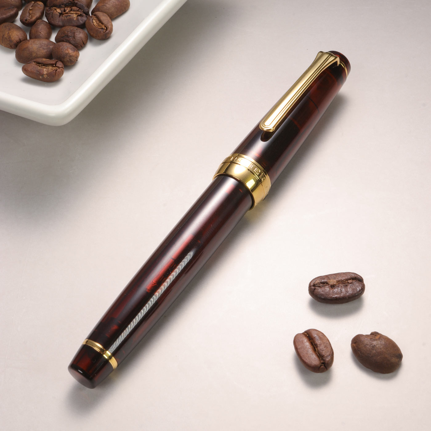 Pen with gold accents on a light surface with coffee beans