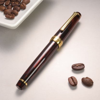 Pen with gold accents on a light surface with coffee beans