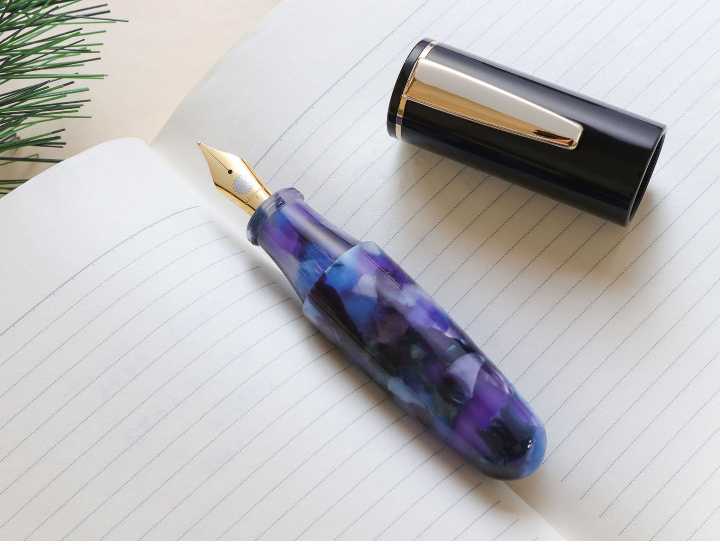 Wancher Pochaco Midnight Violet fountain pen with a purple, blue, and black design on a notebook page with gold colored nib