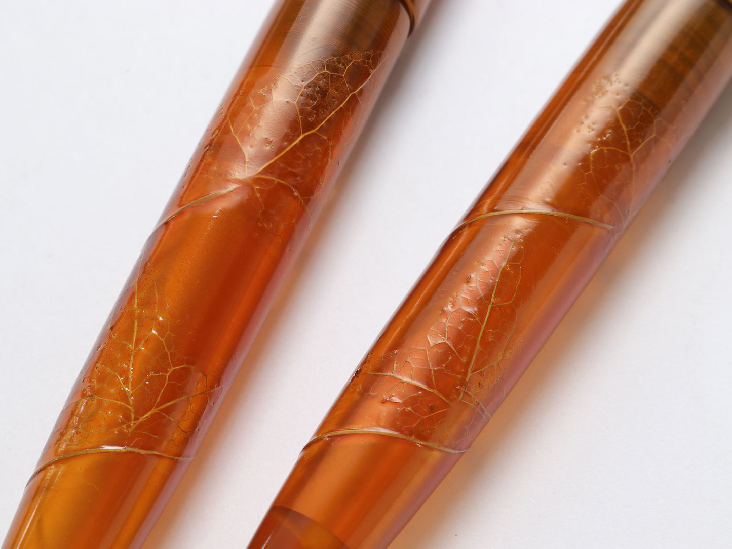 Close up two amber-colored pens with leaf-like patterns on a white background | Wancher Fountain Pen Urushi Tamesukashi Kiei