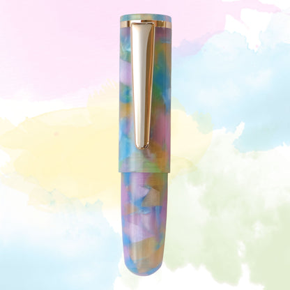 A single pen centered against a pastel watercolor background. The pen has an iridescent marbled pattern with pastel rainbow tones and gold metal clip.
