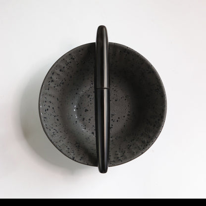 Black speckled ceramic bowl with a black buffalo horn pen on a white background