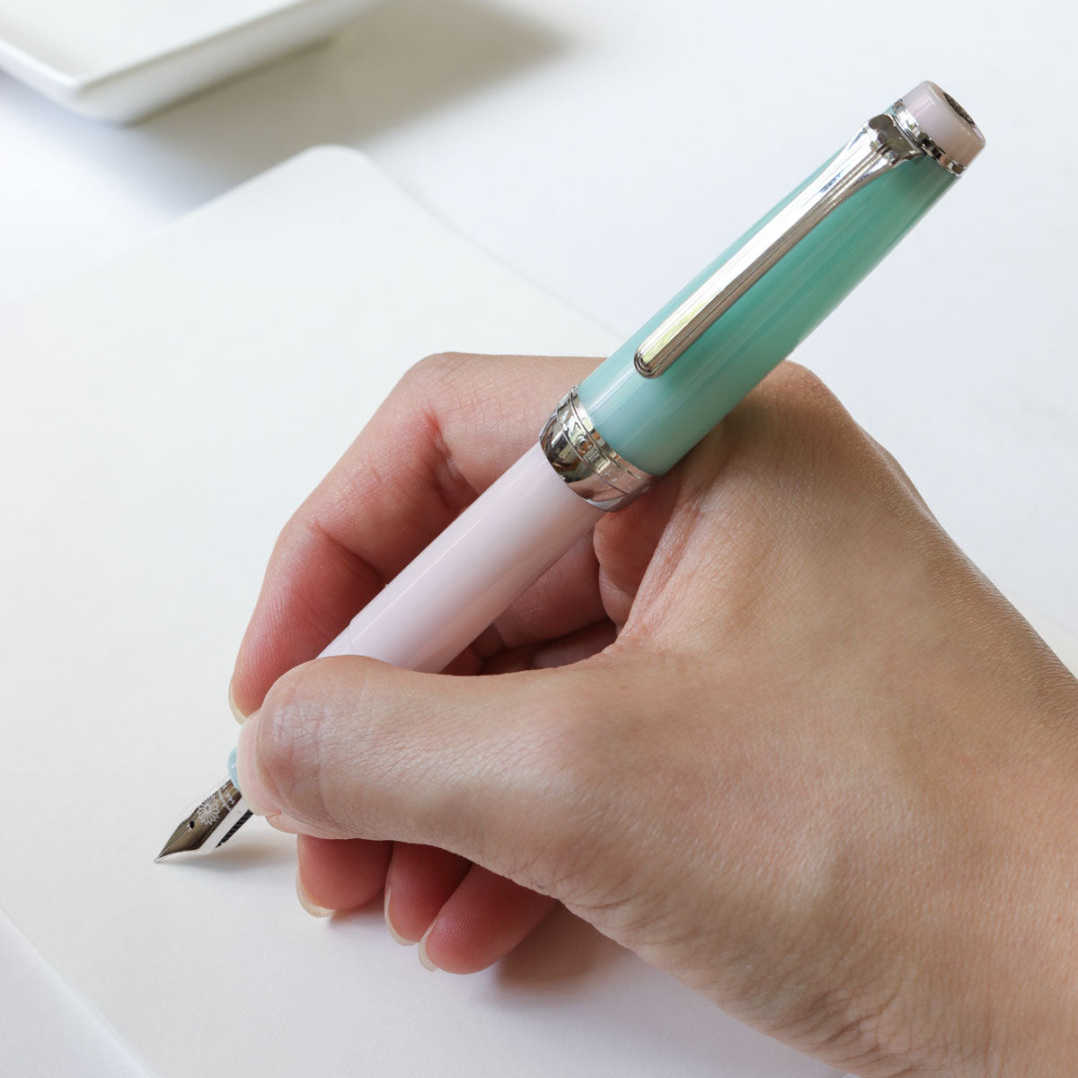 Hand holding a light blue pen on a white surface